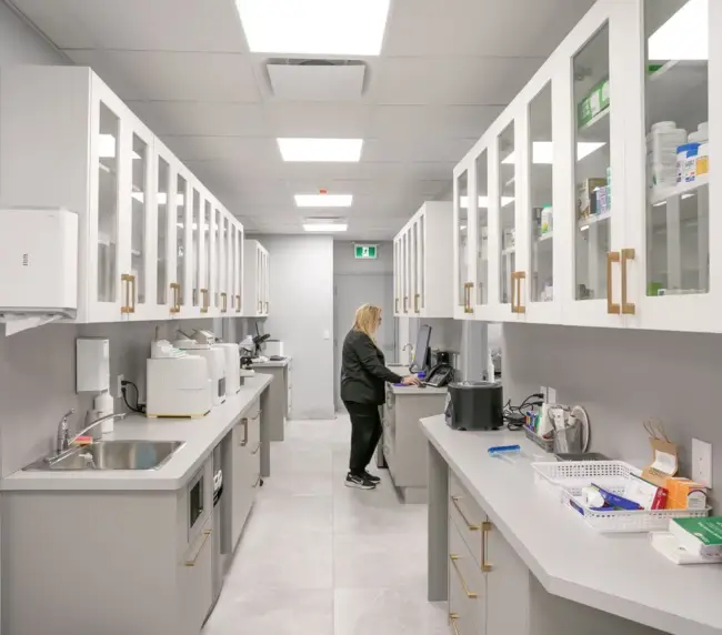 Lab technician at a workbench in a clean, white medical lab with glass-front cabinets and equipment nearby.