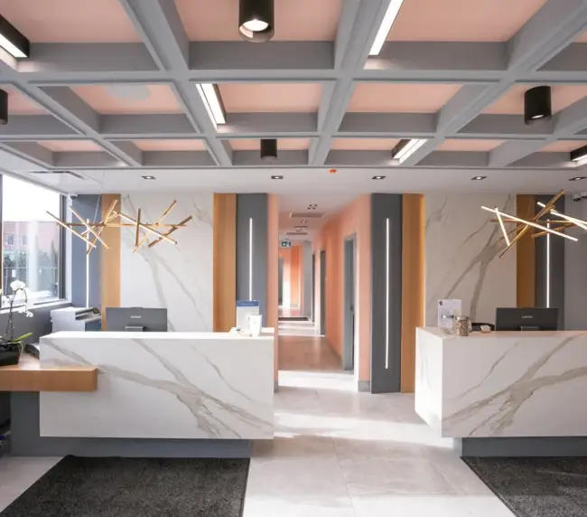 Reception area with white marble counters, peach and gray walls, and geometric pendant lights; hallway leading to offices.